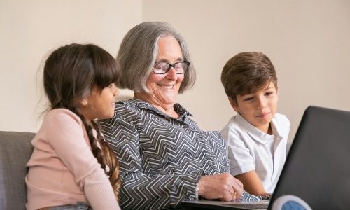 Grandma working the laptop next to two children smiling.